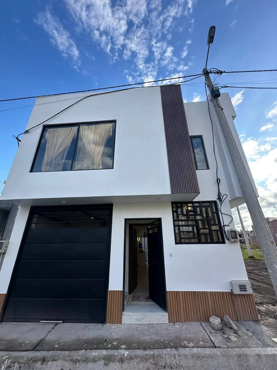 Fachada moderna en blanco y madera de una casa del proyecto Los Prematuros, Riobamba